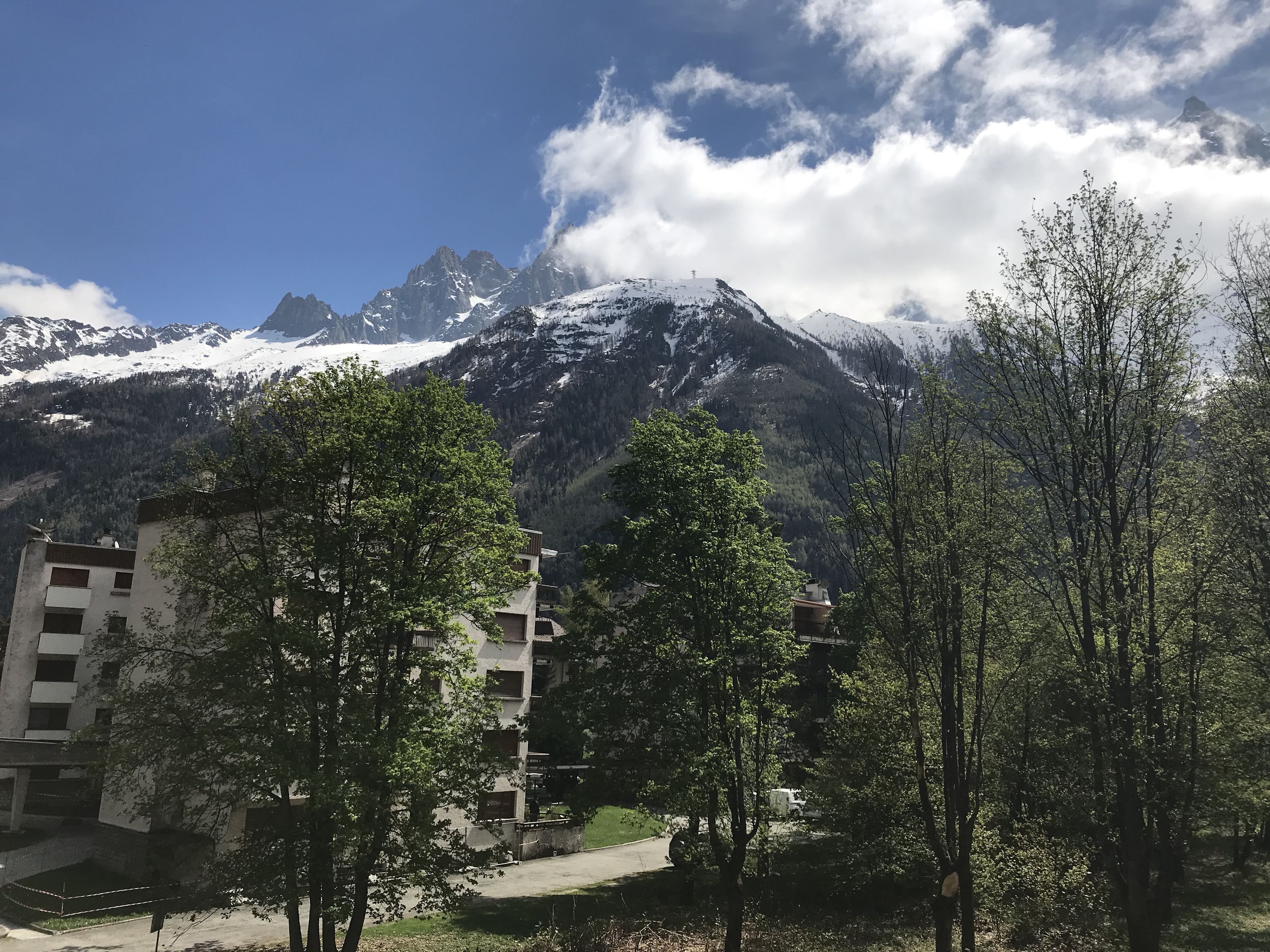 Un paysage montagneux avec des sommets enneigés, un ciel dégagé et un mélange d’arbres et de bâtiments.