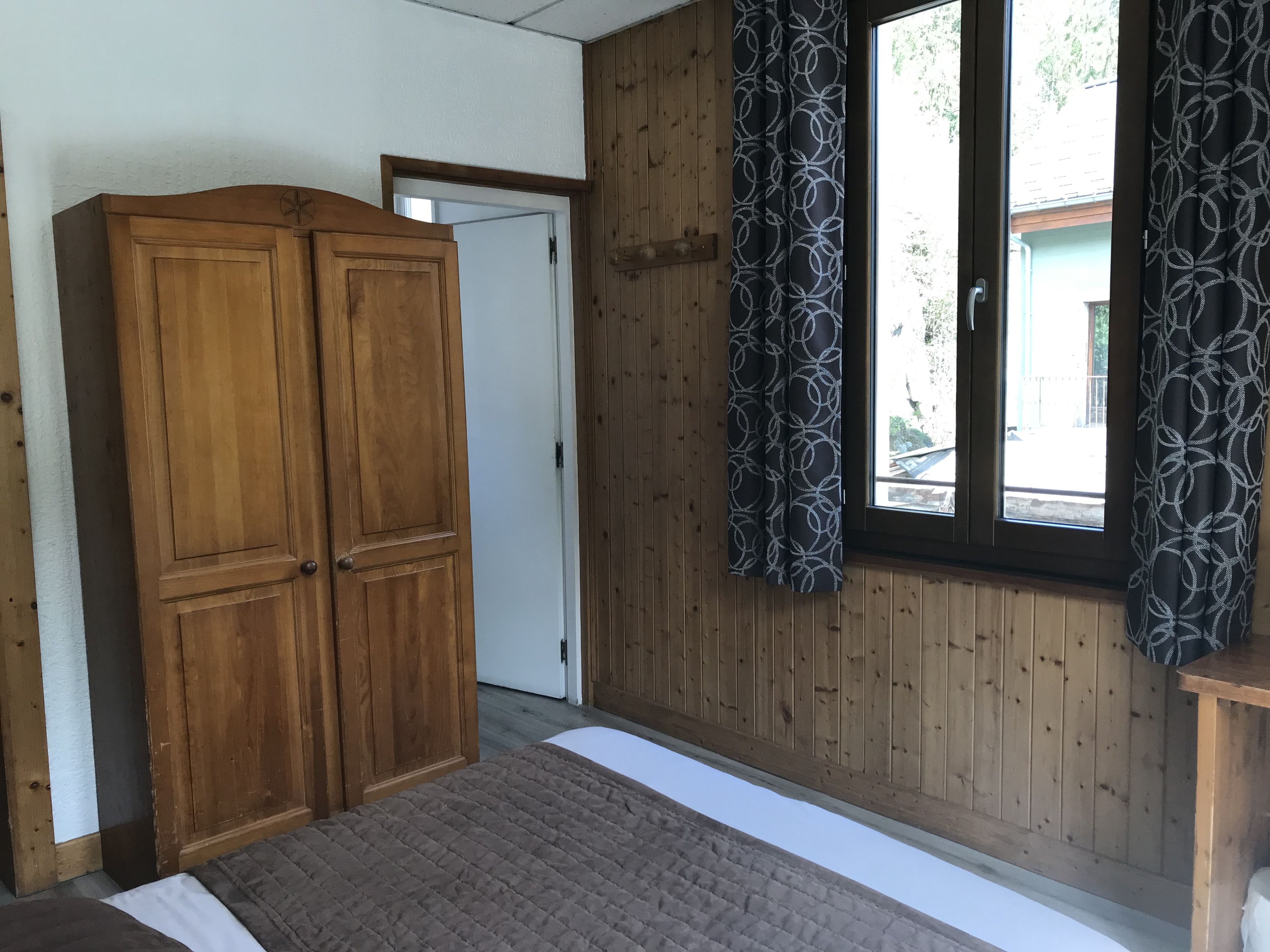 Una stanza con pareti in legno, un armadio grande, un letto e una finestra con tende a motivi.