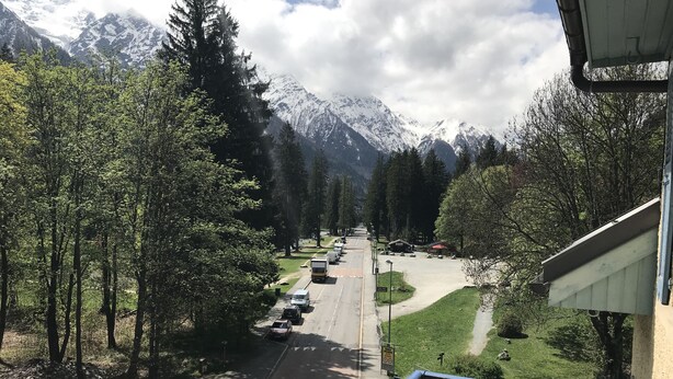 A mountain road with parked vehicles, trees, and a building with a balcony. - Hôtel des Lacs (Chamonix-Mont-Blanc)