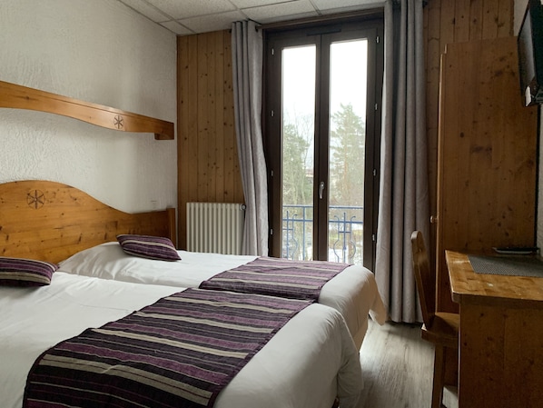 A hotel room with two beds, a wooden headboard, a radiator, a balcony with a metal railing, and a wooden desk. - Hôtel des Lacs (Chamonix-Mont-Blanc)
