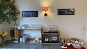 A breakfast buffet setup with various food items, a coffee machine, and a wall-mounted lamp. - Hôtel des Lacs (Chamonix-Mont-Blanc)