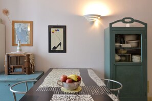 A dining table with a bowl of fruit, a vintage radio, and a framed picture on the wall.