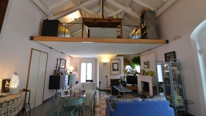 Una sala de estar acogedora con techo alto, un sofá, una mesa de comedor y una chimenea.