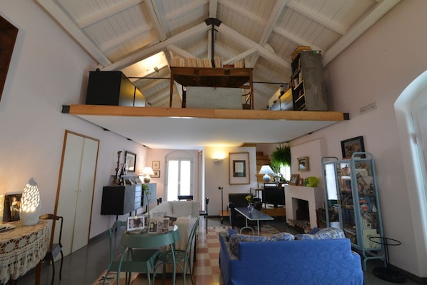A cozy living room with a high ceiling, a sofa, a dining table, and a fireplace.