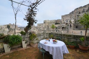 A rooftop terrace with a table set for dining, surrounded by potted plants and overlooking a historic cityscape.