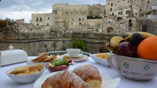Una mesa con croissants, pasteles y un bol de fruta frente a un edificio histórico.