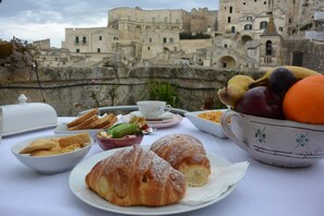 A table with croissants, pastries, and a bowl of fruit in front of a historic building. - Da Ida - In Lak' Ech (Matera)