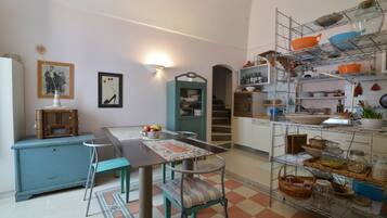 A kitchen with a dining table, chairs, a blue cabinet, and a metal shelf unit with various kitchen items.