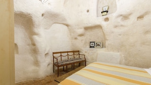 Una habitación con una cama, un banco y una lámpara fijada a la pared.