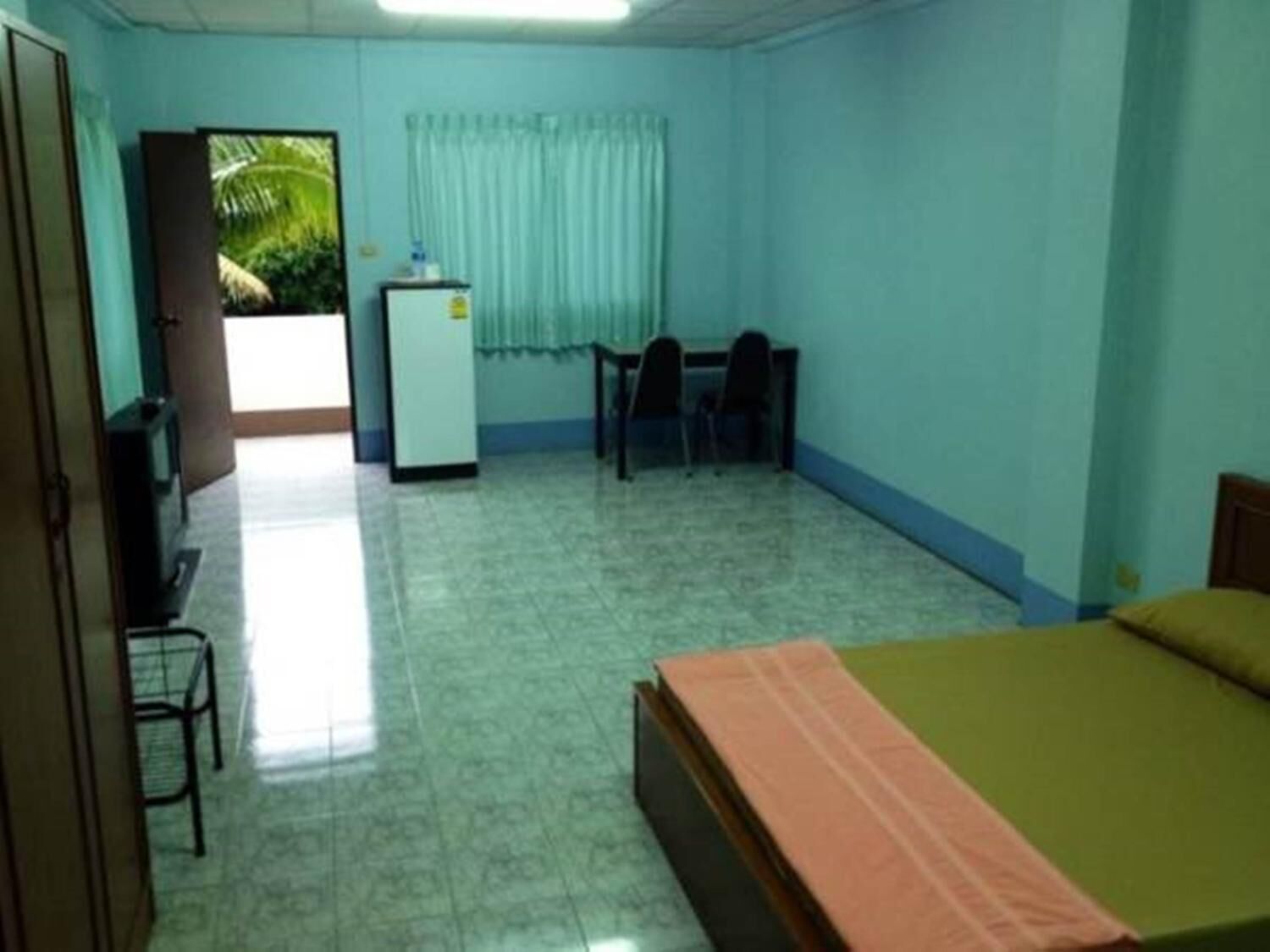 A small, clean room with a bed, a desk, and a refrigerator.