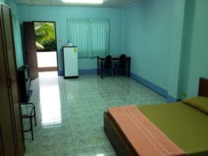 A small, clean room with a bed, a desk, and a refrigerator. - Sunshine Mansion (Kabin Buri)