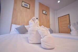 Una cama bien tendida con dos toallas blancas dobladas al pie, un cabecero de madera y una puerta de madera al fondo.