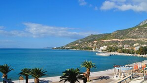 A coastal view with a beach, palm trees, and a mountainous backdrop. - Grand Hotel Loutraki (Loutraki-Agioi Theodoroi)