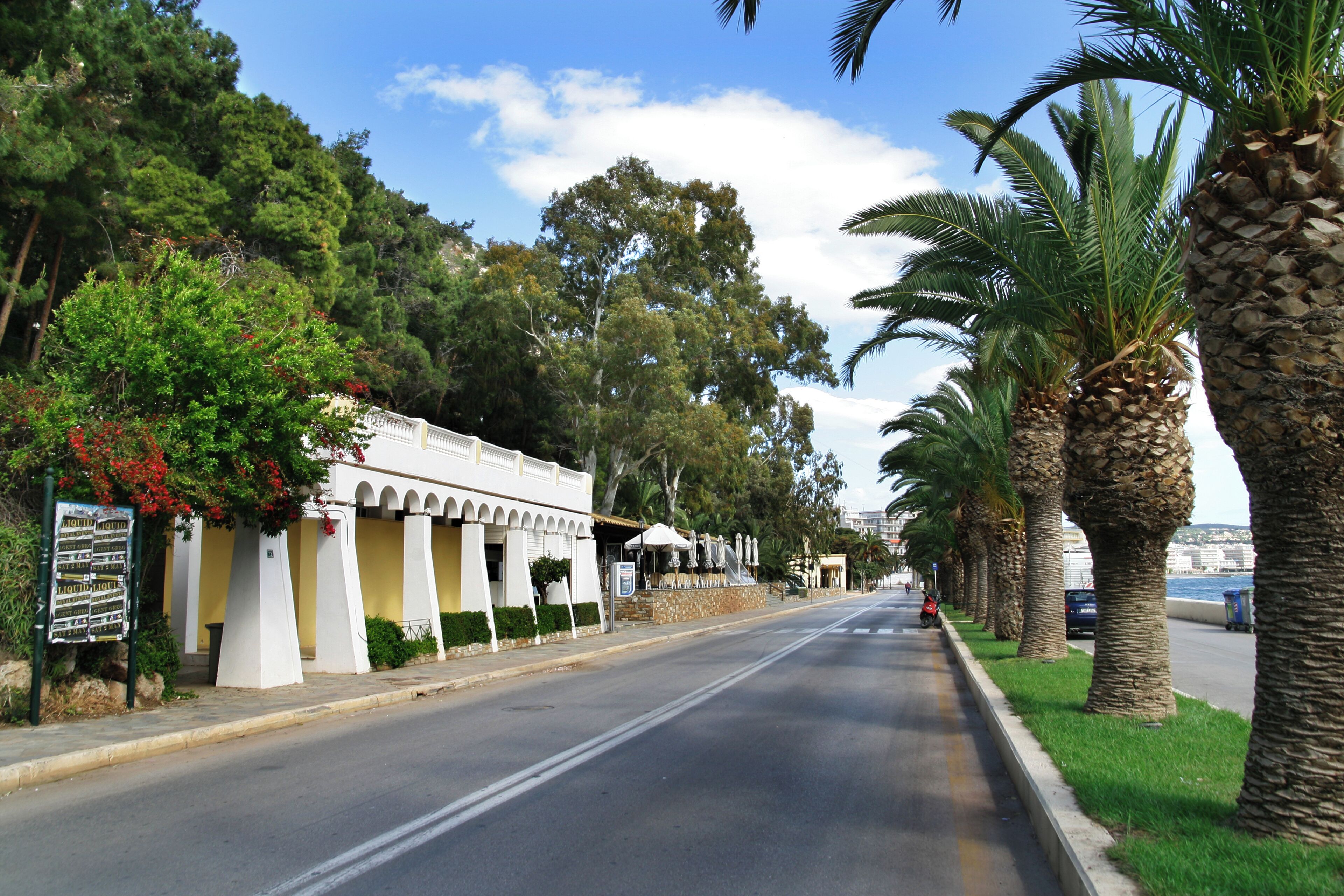 A street lined with palm trees and a building with a white facade and arches.
