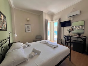 A hotel room with a bed, a desk, a chair, a TV, and a window with curtains. - Grand Hotel Loutraki (Loutraki-Agioi Theodoroi)