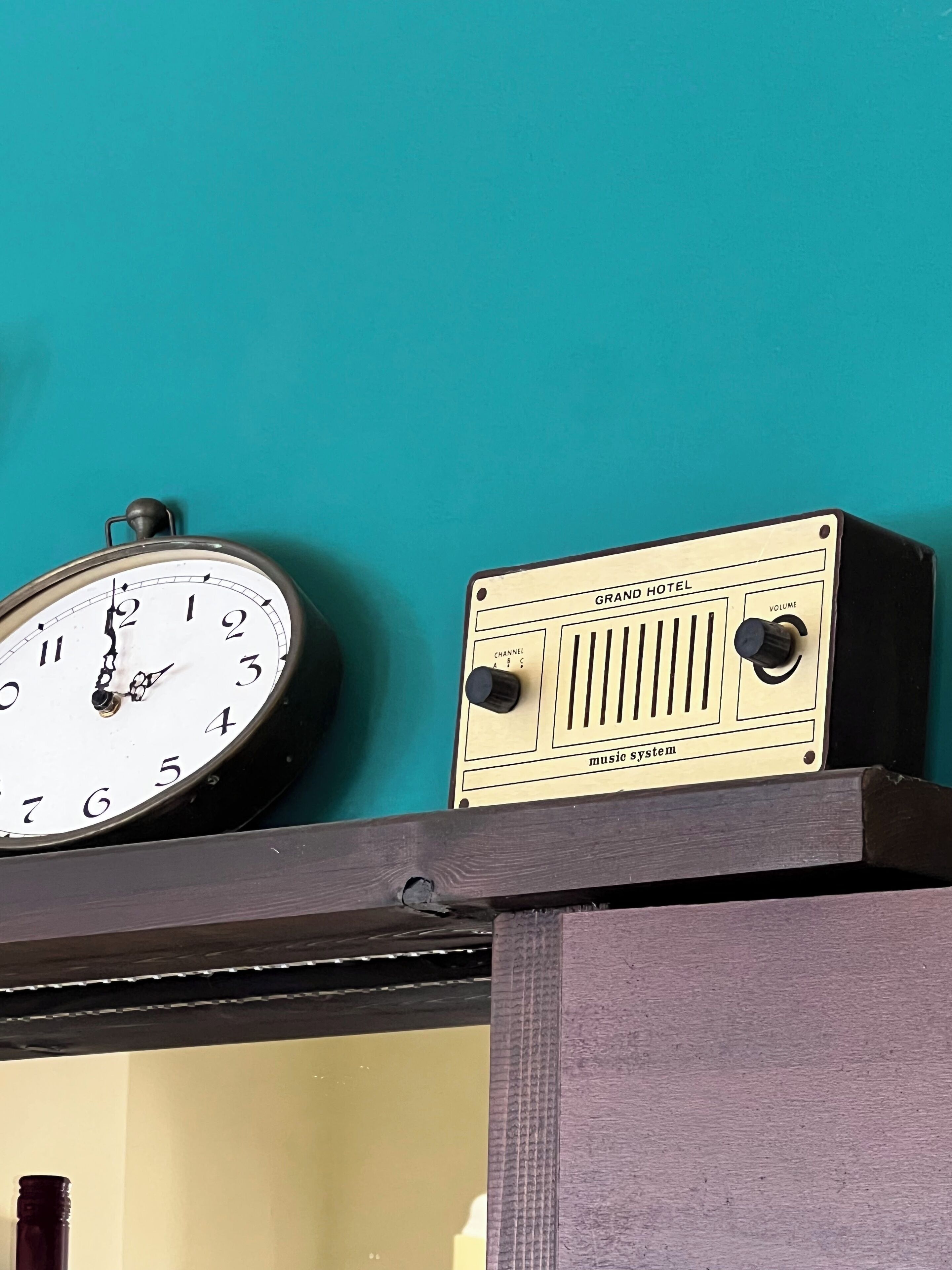 A clock and a radio on a shelf against a teal wall.