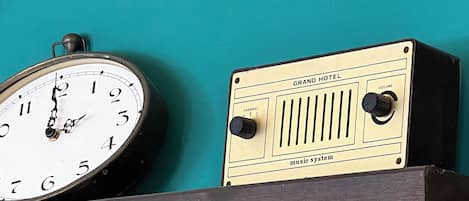 A clock and a radio on a shelf against a teal wall.