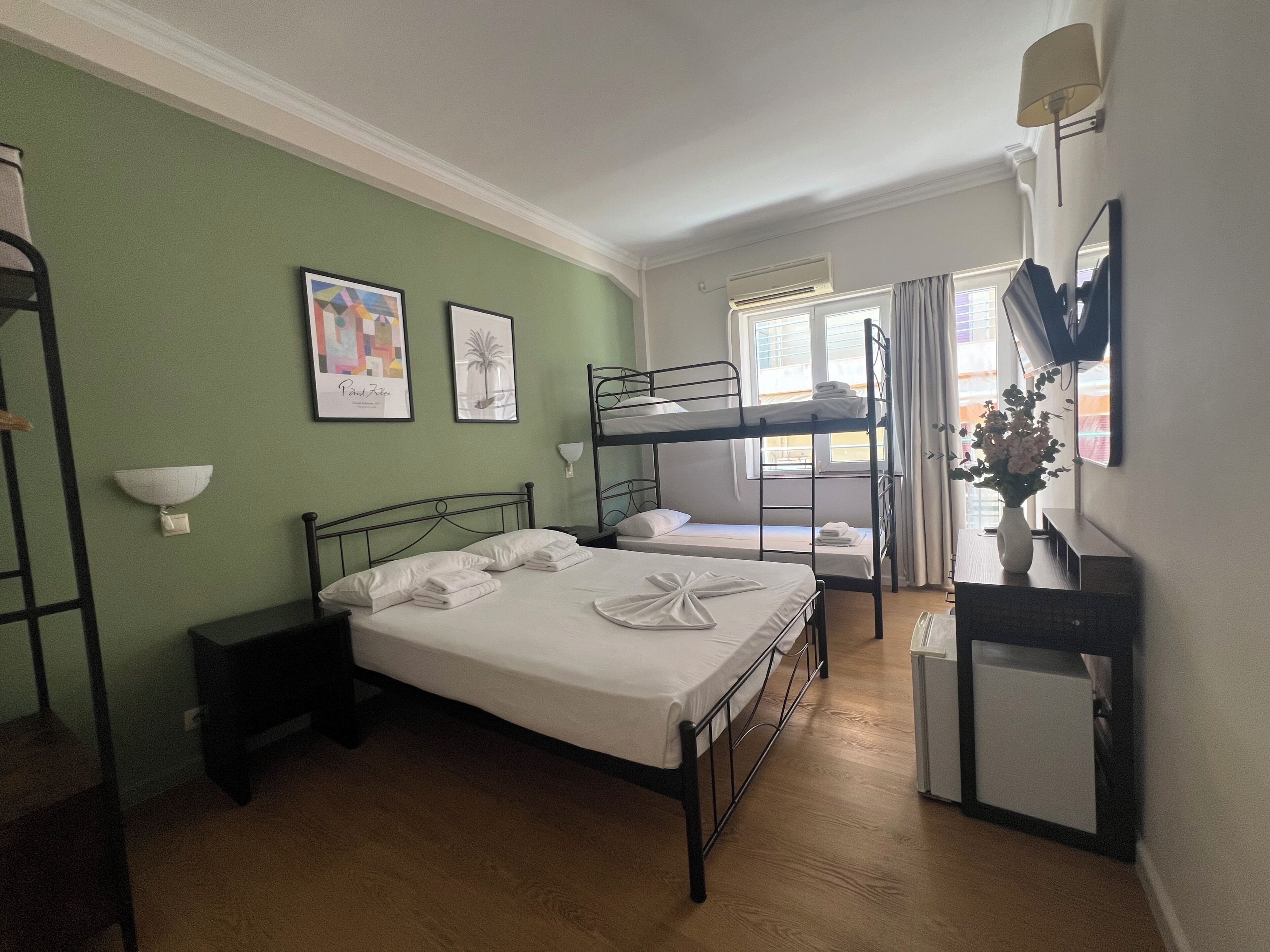 Une chambre d’hôtel avec des lits superposés, un bureau avec un miroir, un vase de fleurs et des œuvres d’art accrochées aux murs.