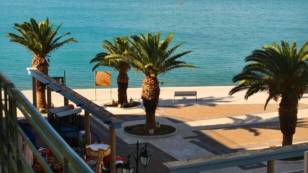 A coastal promenade with palm trees, a bench, and a carousel. - Grand Hotel Loutraki (Loutraki-Agioi Theodoroi)