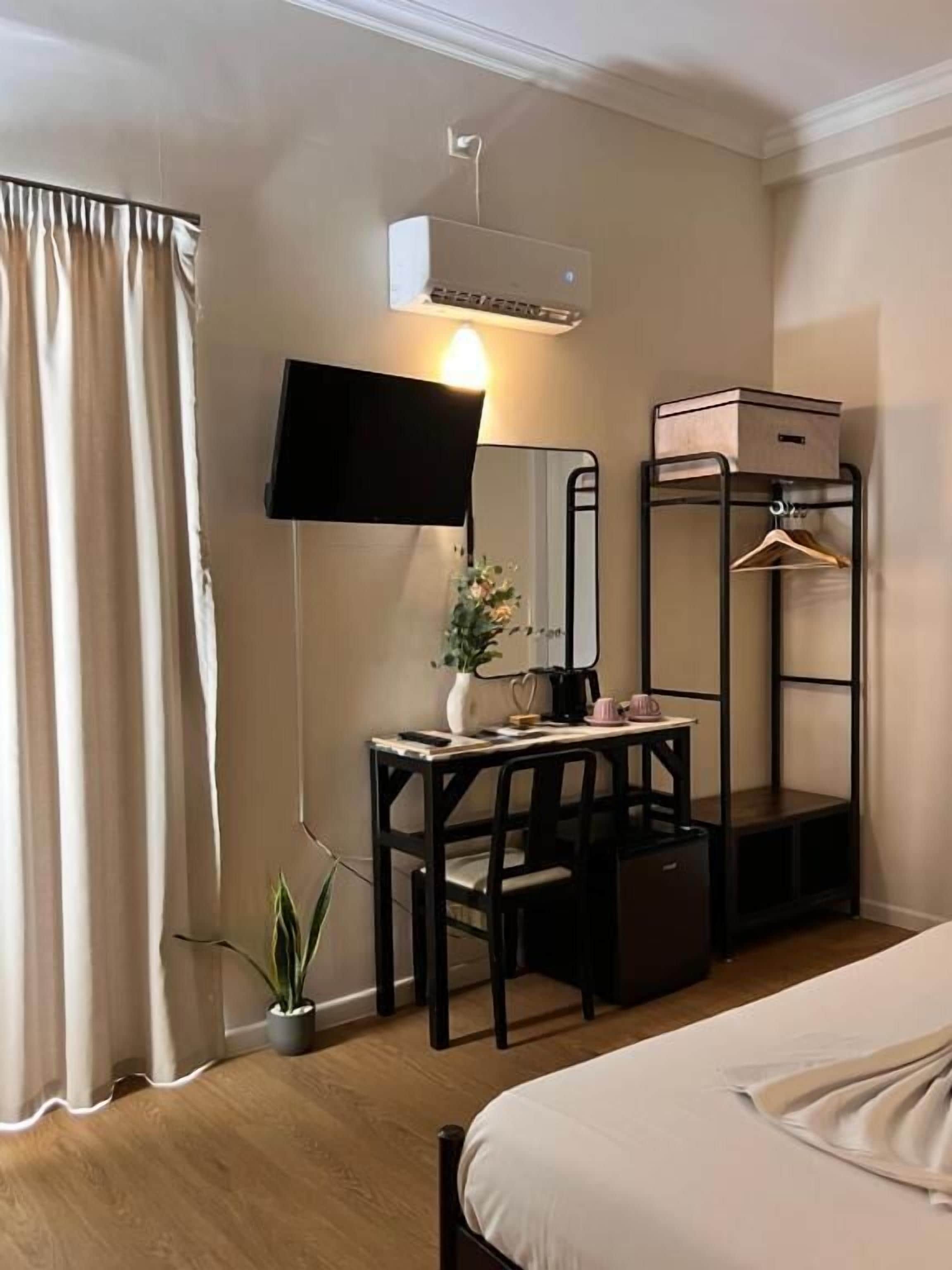 Een hotelkamer met een bed, een bureau met stoel, een spiegel, een televisie, een kledingkast en een kamerplant.