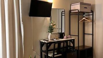 Een hotelkamer met een bed, een bureau met stoel, een spiegel, een televisie, een kledingkast en een kamerplant.