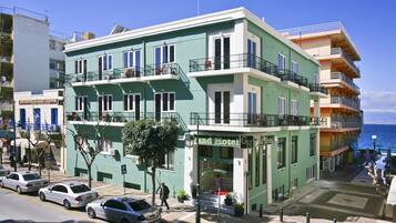 A multi-story hotel with balconies, a visible entrance, and a parking area.