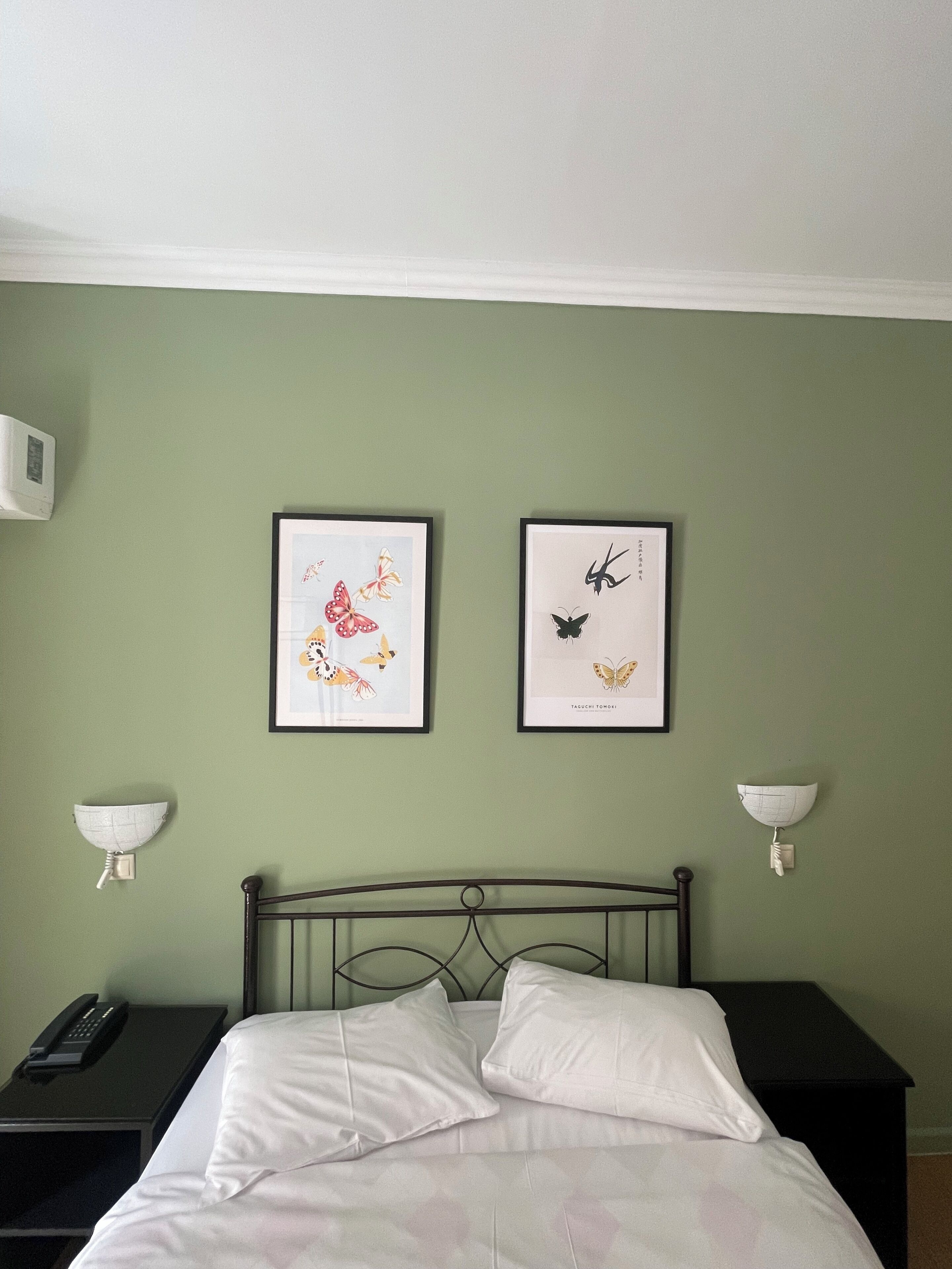 A bedroom with a bed, two framed butterfly artworks, bedside lamps, and a telephone on the nightstand.