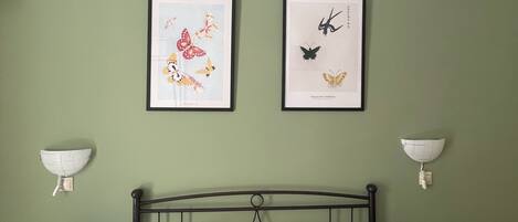 A bedroom with a bed, two framed butterfly artworks, bedside lamps, and a telephone on the nightstand.