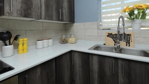 Uma cozinha com armários de madeira escura, bancada branca e uma janela com persianas.