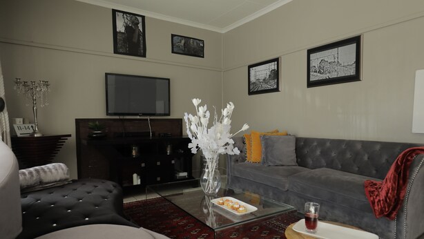 Uma sala de estar moderna com um sofá cinzento, uma mesa de centro de vidro e uma TV de tela plana na parede.
