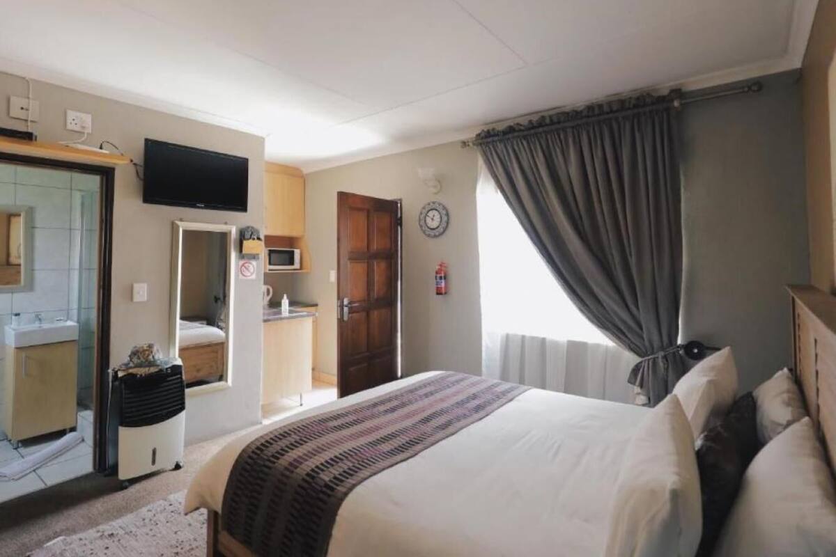A bedroom with a bed, a TV, a bathroom, and a door leading to a kitchen.