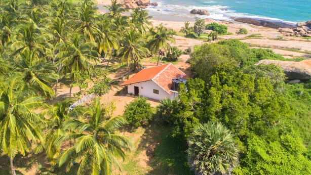 A coastal property with a white building, lush greenery, and a beach. - Redhill Yala (Kirinda)