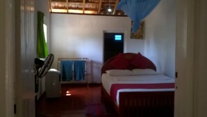A bedroom with a bed, a fan, a heater, and a door leading to another room. - Redhill Yala (Kirinda)