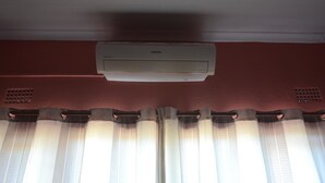 A ceiling-mounted air conditioner in a room with red walls and a window with vertical blinds.