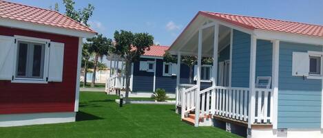 A row of small, single-story cabins with red and blue exteriors, white railings, and a well-maintained lawn.