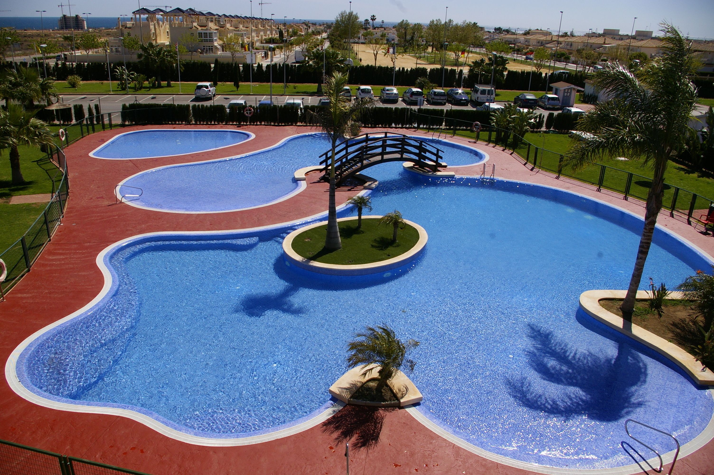 A large outdoor swimming pool with a bridge and palm trees.