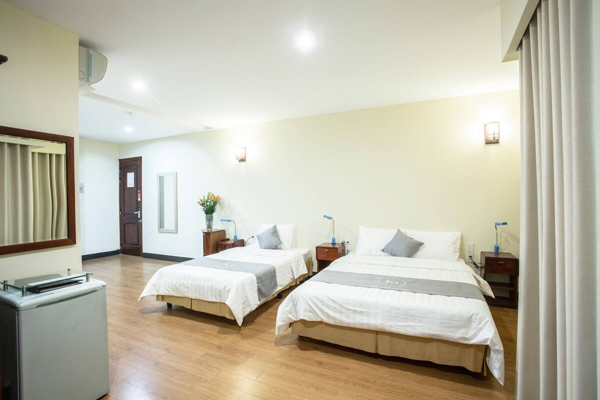 A hotel room with two beds, wooden flooring, a mirror, a small desk, and a nightstand with a lamp.