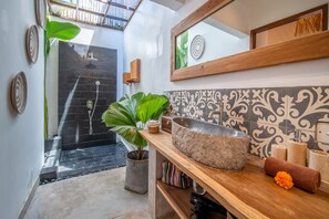 Un baño con un lavabo de piedra grande, un espejo, ducha y plantas decorativas.