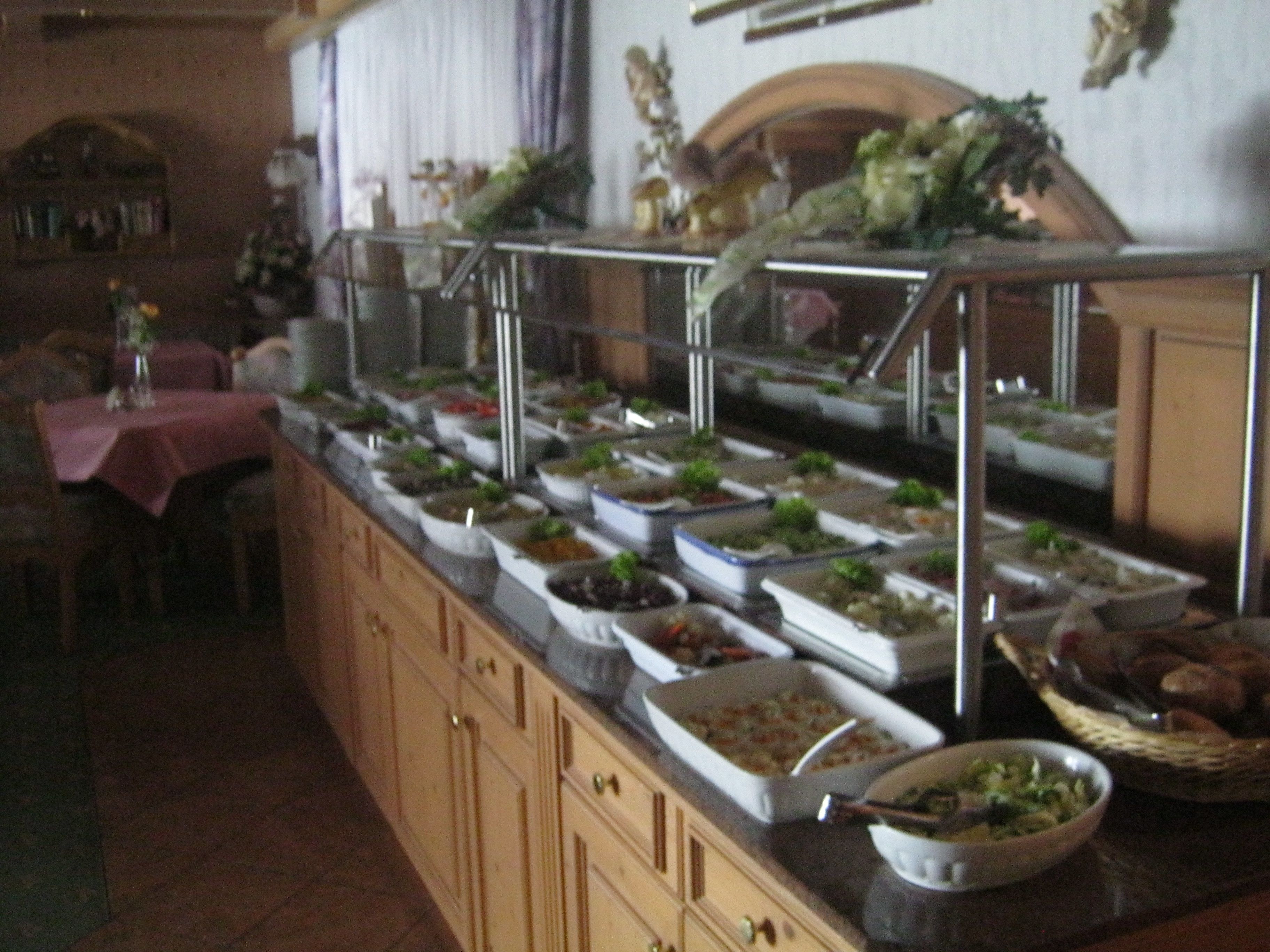 Un buffet avec plusieurs présentoirs de nourriture, un espace repas avec des tables et un mur décoratif.