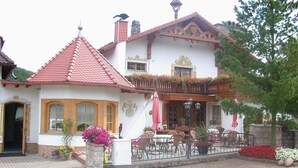 Un edificio tradizionale con tetto in tegole rosse, un balcone fiorito e posti a sedere all'aperto.
