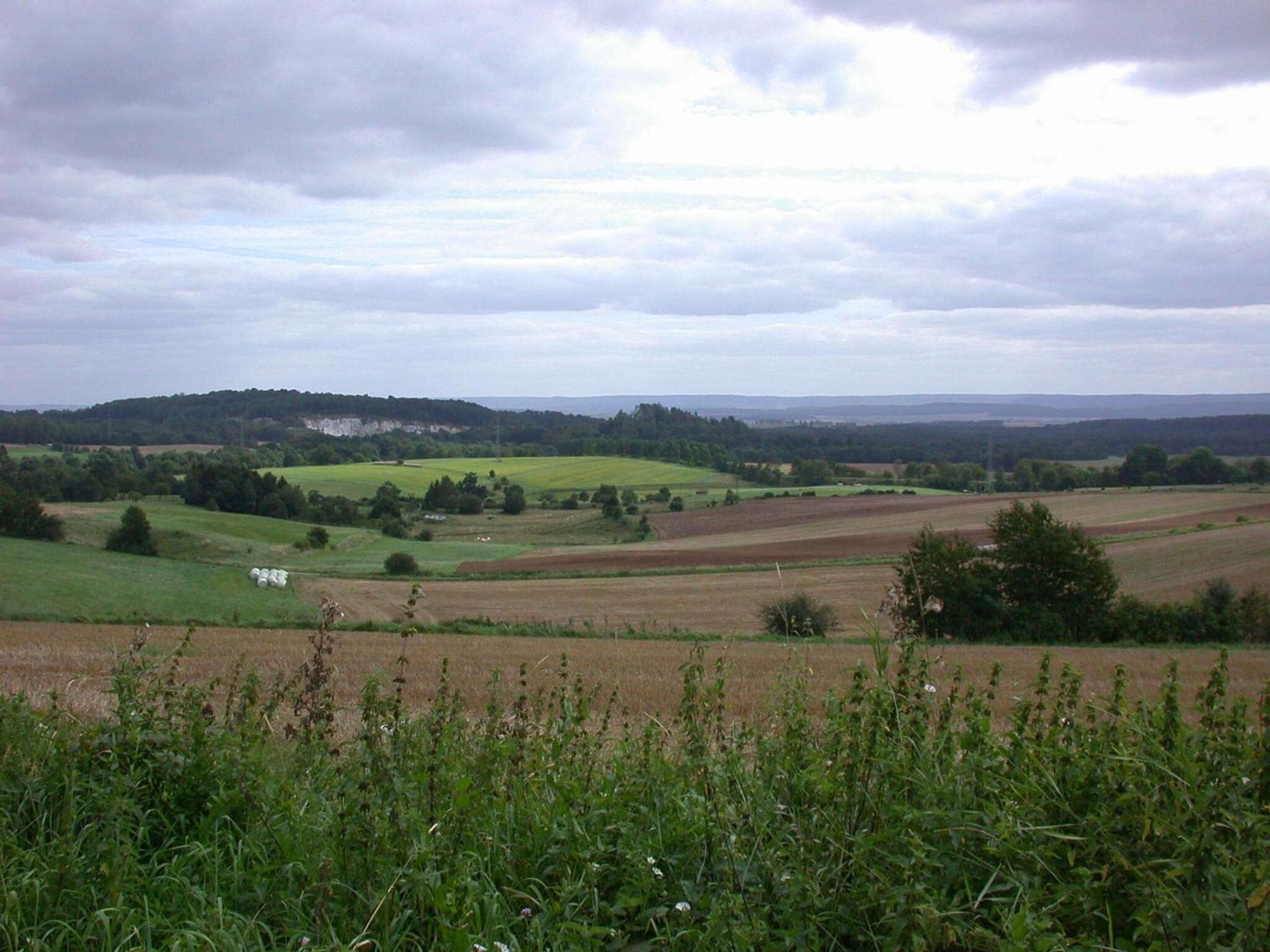 A rural landscape with fields, a small building, and rolling hills in the distance.