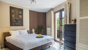 Quarto moderno com uma cama grande, uma mesinha de cabeceira com um vaso e vista para o exterior através de uma janela.