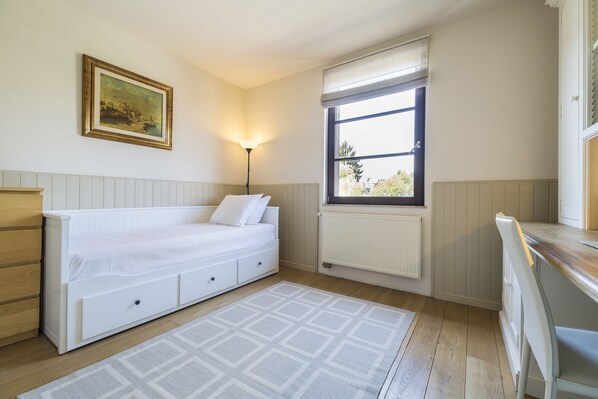 Une chambre à coucher avec un lit, un radiateur, une fenêtre, une lampe et un tableau au mur.
