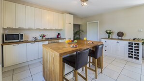 Cozinha moderna com armários brancos, ilha de madeira e adega embutida.