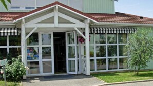 Ein Gebäude mit heller Fassade, rotem Ziegeldach und einem überdachten Eingang mit Glasüren.