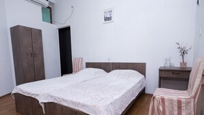 A bedroom with a bed, a wardrobe, a chair, and a small table with a vase. - Tiflisi Guest House - Hostel (Tbilisi)