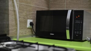 A kitchen with a black microwave oven on a green countertop, a gas stove, and a white electrical outlet on the wall. - Tiflisi Guest House - Hostel (Tbilisi)