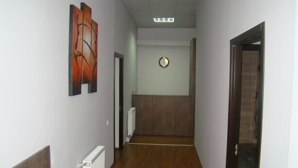 A hallway with a wooden floor, a radiator, a clock on the wall, and a door on the right. - Tiflisi Guest House - Hostel (Tbilisi)