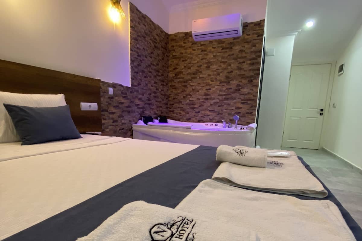 A hotel room with a large bed, a bathtub, and a wall with a brick pattern. There are towels with the hotel's logo on them.
