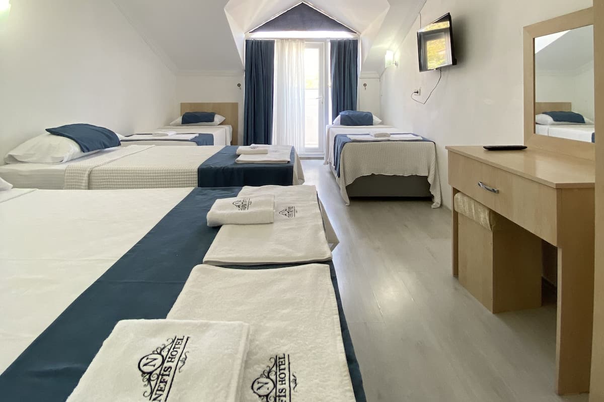 A hotel room with three beds, a desk, and a large window with curtains.